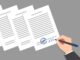 Stack of documents and hand of person wearing business suit, signing and stamping them. Concept of signing of new acts, decrees, agreements, political, legal or business relationships