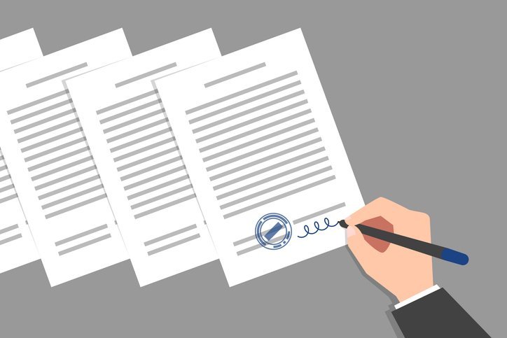 Stack of documents and hand of person wearing business suit, signing and stamping them. Concept of signing of new acts, decrees, agreements, political, legal or business relationships
