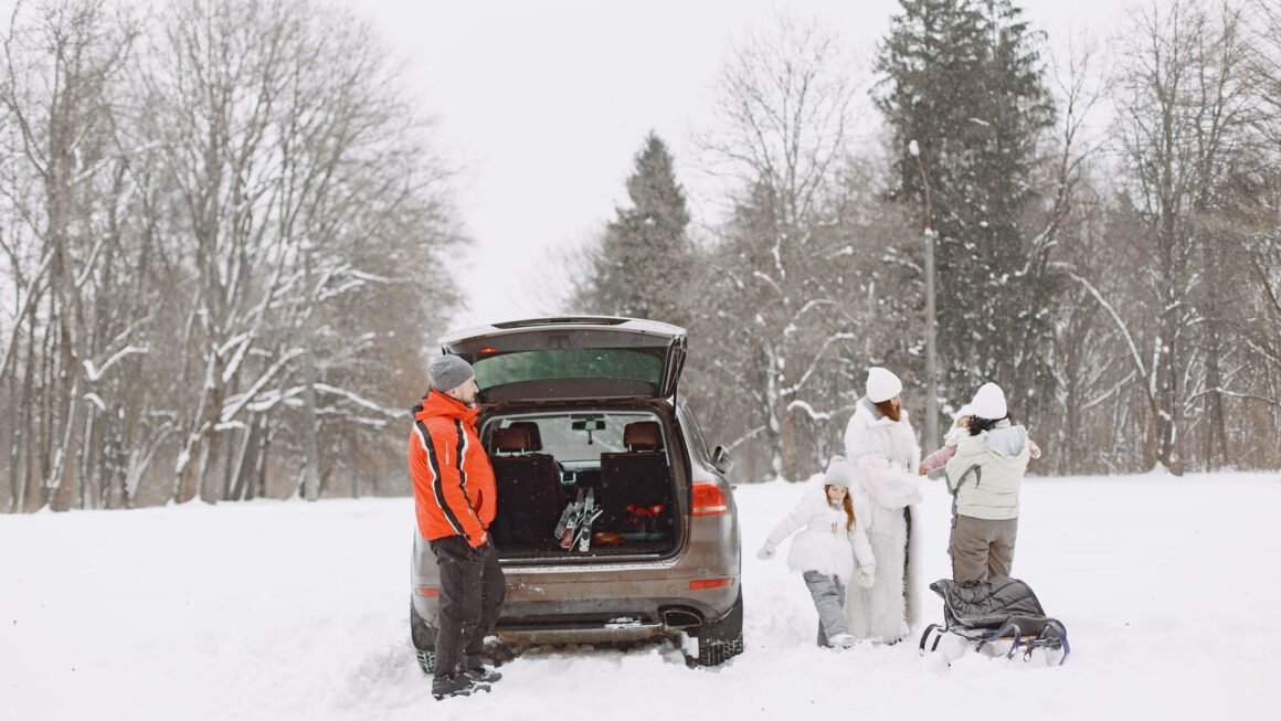 Family in winter gear preparing for outdoor adventure with SUV in snow-covered landscape.